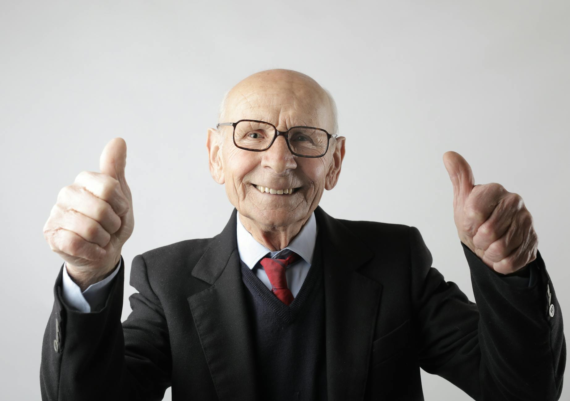 positive senior man in eyeglasses showing thumbs up and looking at camera